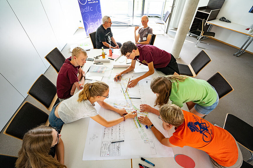 Pedal Plausch Gruppe von Menschen an einem Tisch auf dem ein Lageplan liegt.