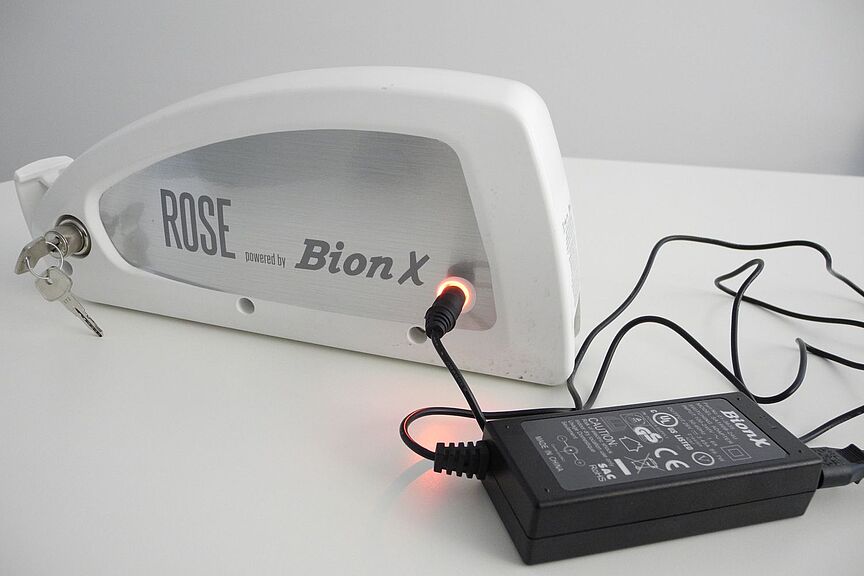 Alter Elektrorad-Akku Ein Elektrorad-Akku steht auf einem Tisch und ist am Netzteil angeschlossen.