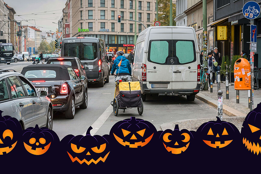 Halloweenreife Verkehrssituation Die Straßenszene in Berlin zeigt einen Radfahrer mit gelbem Anhänger, der sich zwischen Autoss seinen Weg bahnt.